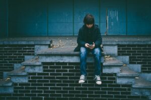 Jovem sentado olhando para o celular com expressão pensativa, representando o coração da geração digital por trás da tela