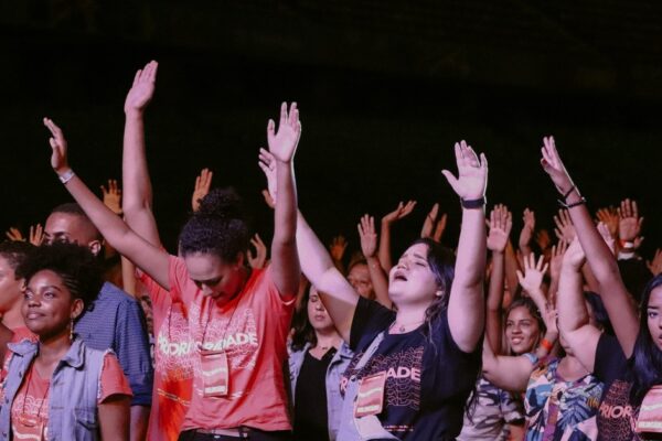 Multidão de adolescentes de mãos levantadas em adoração na Conferência de Adolescentes da Assembleia de Deus