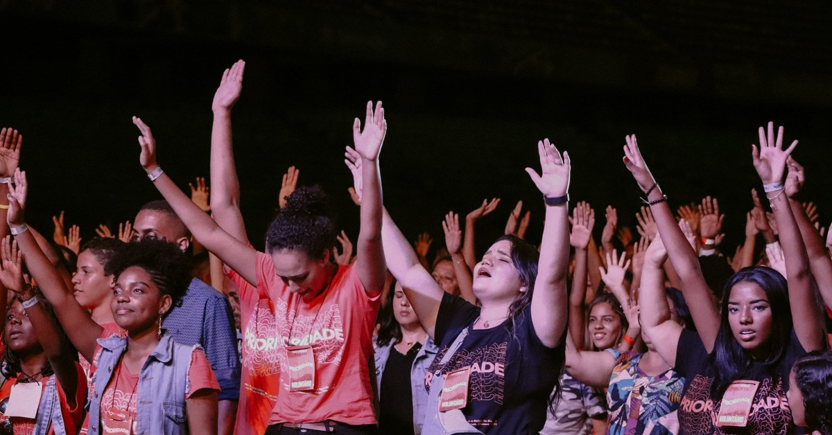 Multidão de adolescentes de mãos levantadas em adoração na Conferência de Adolescentes da Assembleia de Deus