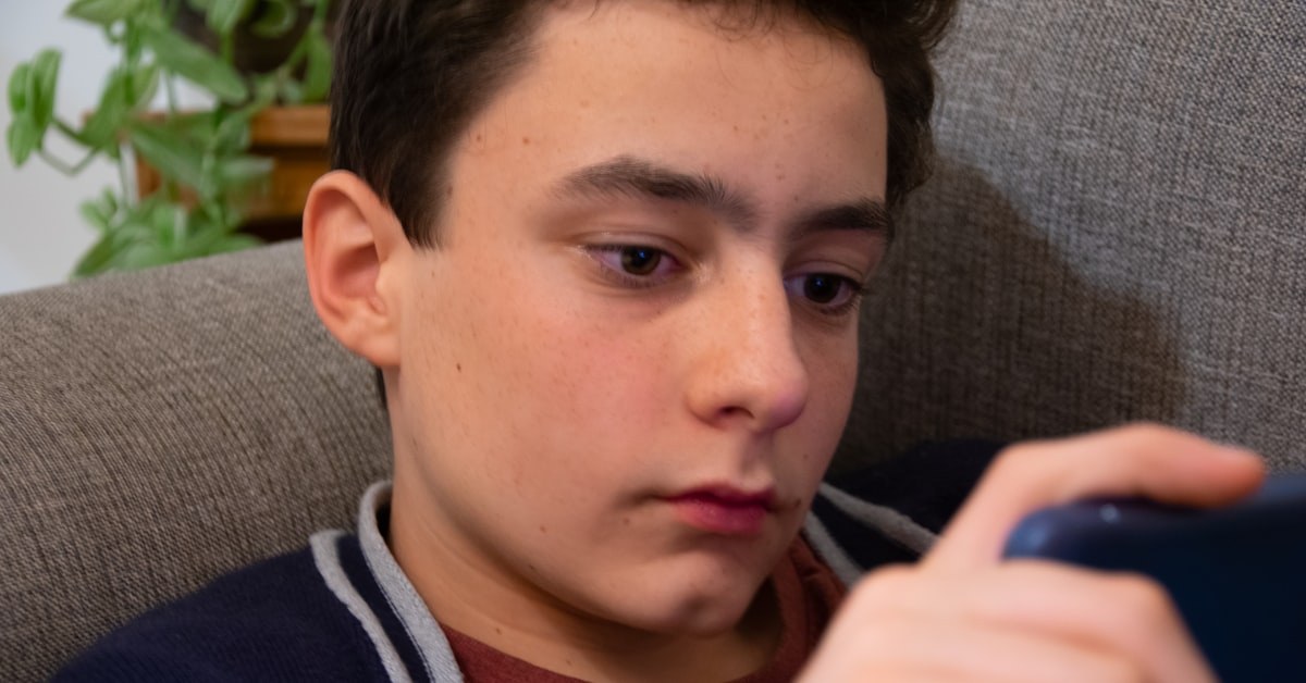 Adolescente olhando o celular com expressão pensativa, representando o coração do adolescente por trás da tela