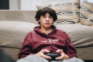 adolescente disperso jogando videogame com o celular ao lado