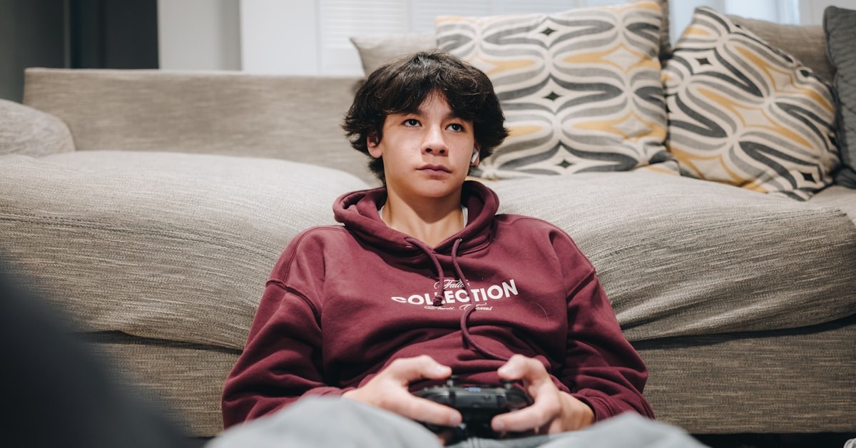 adolescente disperso jogando videogame com o celular ao lado