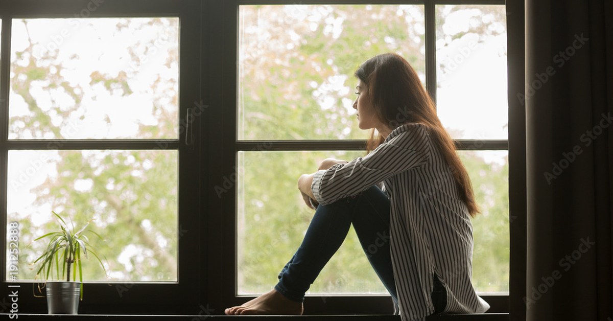 Adolescente sentado sozinho olhando pela janela, representando o isolamento sofrido por vítimas de bullying na infância