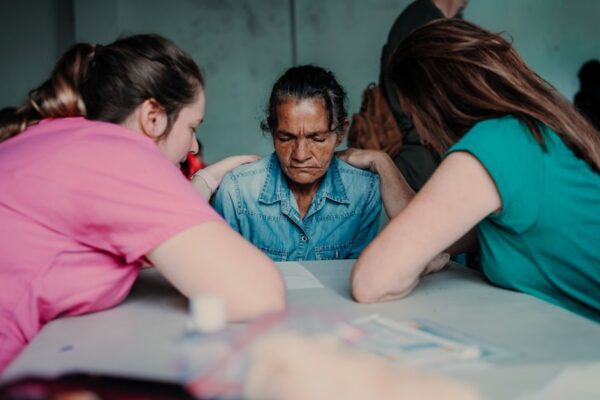 Equipe jovem de viagem missionária orando com as mãos sobre uma moradora local, cena ligada à jovem surda curada em viagem missionária