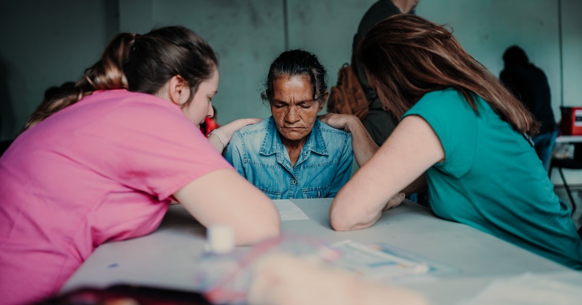 Equipe jovem de viagem missionária orando com as mãos sobre uma moradora local, cena ligada à jovem surda curada em viagem missionária